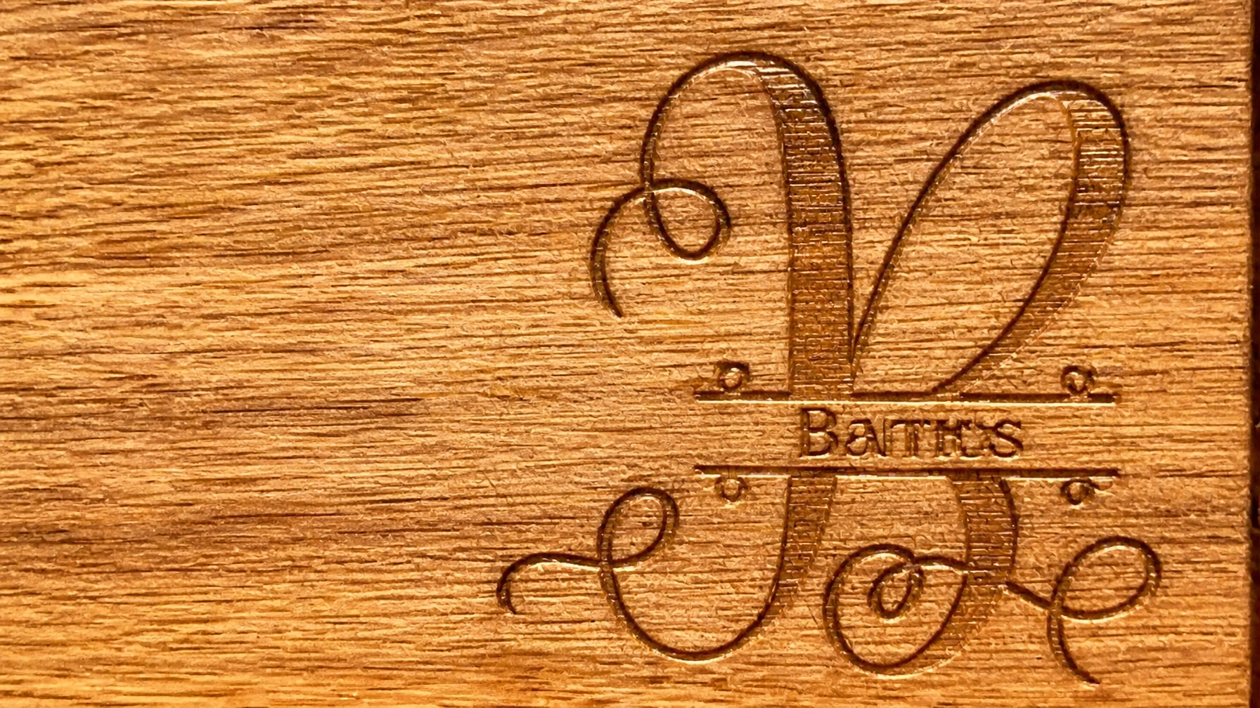 Close-up of intricate laser-engraved family name monogram detail on an acacia wood cutting board